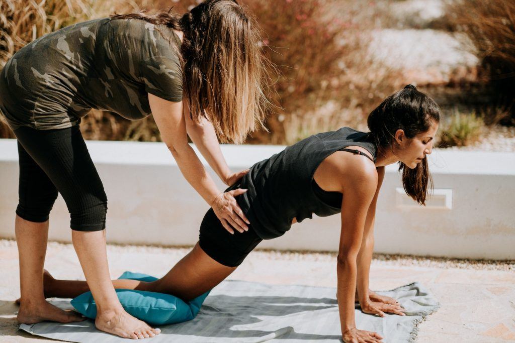 a trainer sharing exercise tips with woman in black tank top and black shorts kneeling on mat