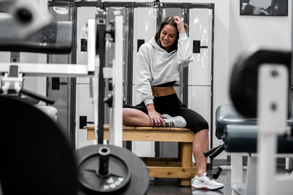 woman in white long sleeve shirt sitting on a brown bench at the gym