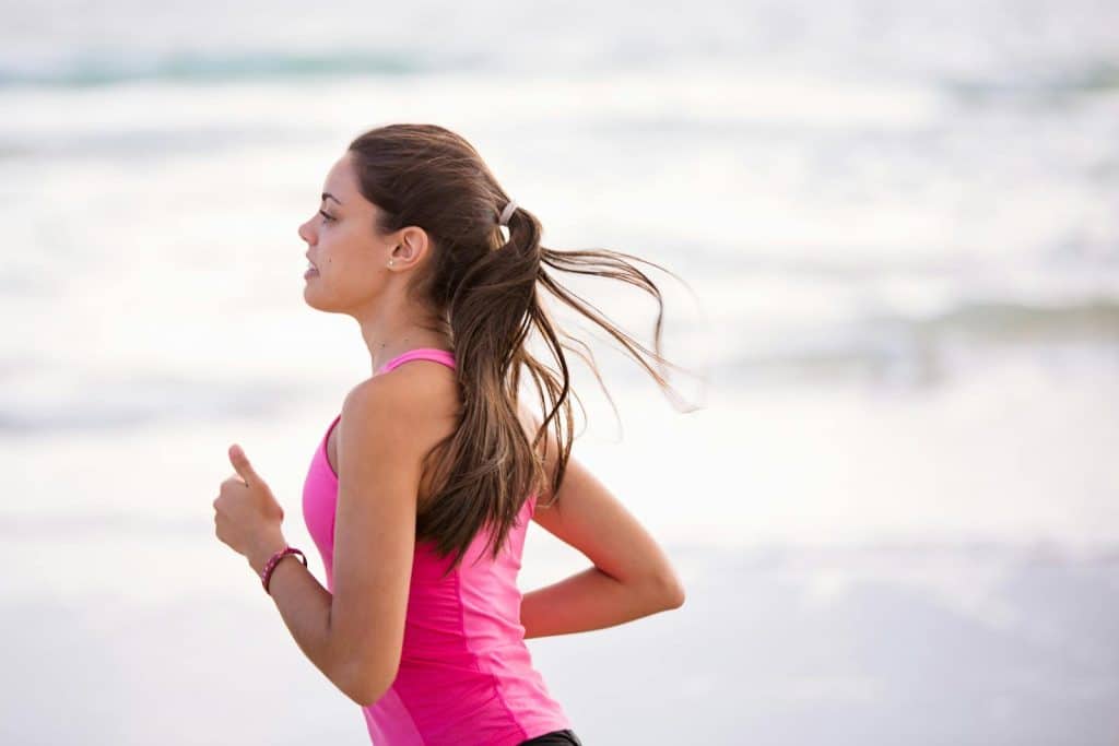 A woman in a pink shirt jogging on the beach after eating her recommended diet