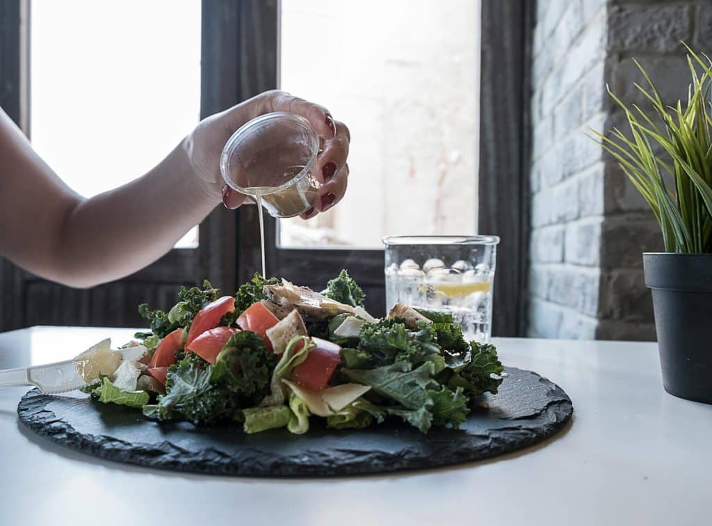A person pouring dressing on a vegetable salad is part of a unique diet strategy everyone is talking about