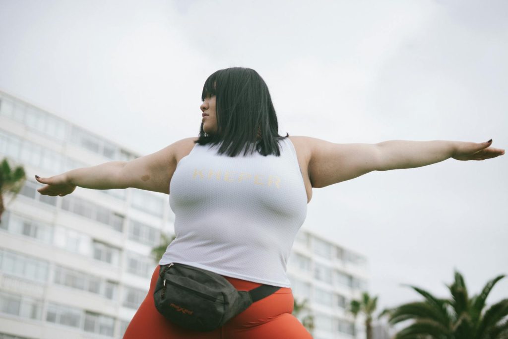 A woman In a white tank top with her arms raised ready for surefire diet and exercise results