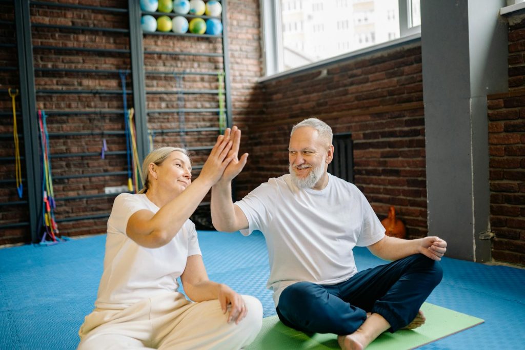 An elderly couple high fiving each other while sitting in the gym